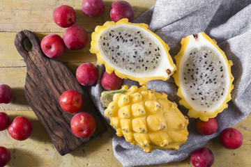 yellow pitahaya or dragon fruit and red plum on wooden background