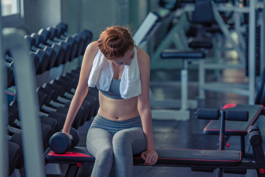 Portrait of cheerful pretty young fitness woman with white towel on her neck relax after exercise at indoor sport gym, beauty and healthy sport concept.