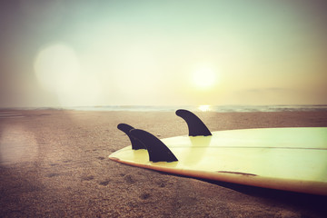 Retro style photo of surfboard on beach at sunset