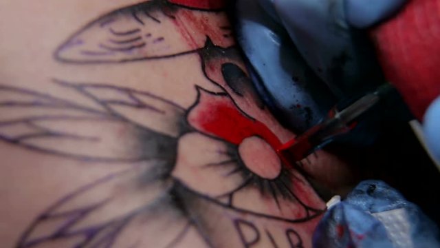 Needle tattoo machines inject a red ink into the skin of a man. Tattoo art on body. Makes a tattoo. Professional tattooist doing tattooing in studio. Close-up.
