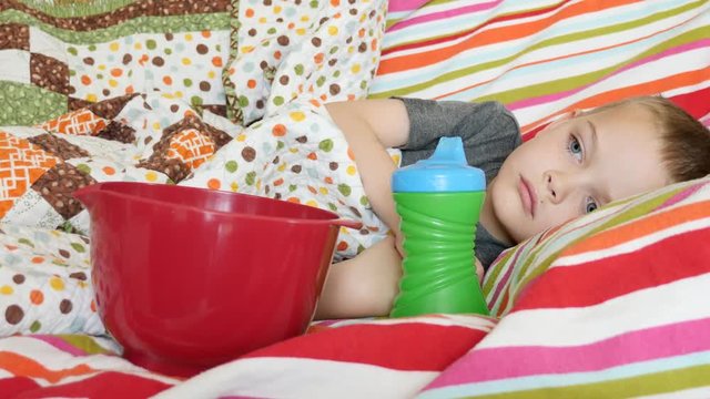 A pore little boy lies sick on the couch with a bowl
