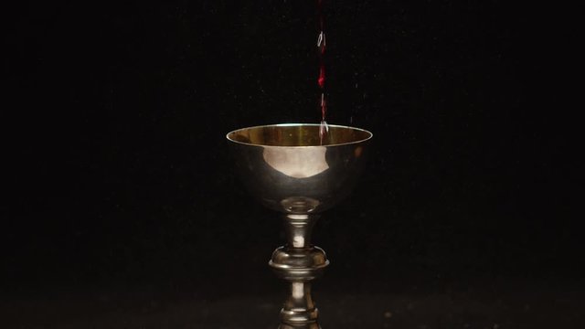 Slow motion wine pouring into golden christian chalice 