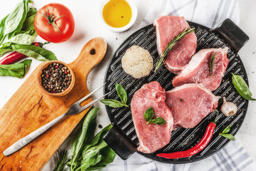 Raw meat, pork steaks with spices, herbs, olive oil, white marble background on grill pan, top view, copy space
