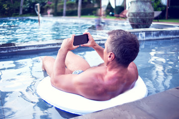 Young man relaxing on the pool, using mobile phone. Work and relaxation