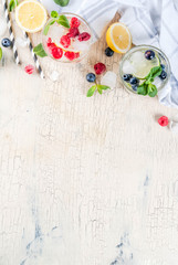 Various berry lemonade or mojito cocktails, fresh iced lemon lime raspberry blueberry infused water, summer healthy detox drinks light background copy space above