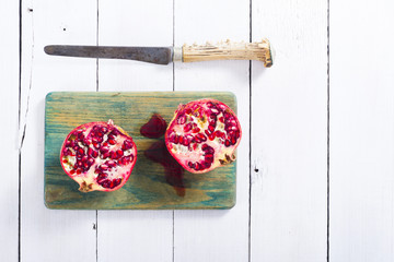 pomegranates on green cutting board, old knife on white wood table background