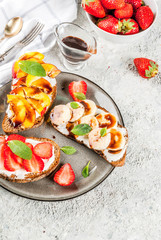 Healthy summer breakfast snack, Rye toast sandwiches with fruit and berries - strawberry, peach, banana - with chocolate sauce, light concrete background copy space