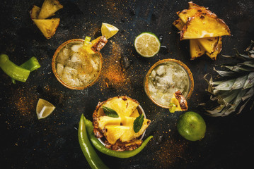 Mexican beverage, spicy margarita cocktail with pineapple and jalapeno and lime, dark blue background copy space top view