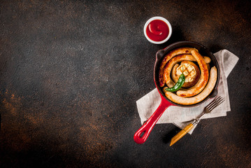 Homemade grilled beef and chicken sausages in red cast iron frying pan, with ketchup, dark background copy space above