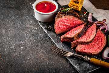 Fresh grilled beef, homemade bbq meat medium rare, on black stone cutting board, with spices, dark background, copy space