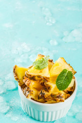 Slice of pineapple in white bowl and mint leaves, on light blue background with ice, copy space
