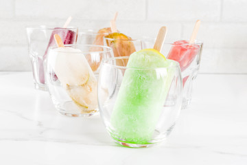 Summer party food ideas, frozen boozy alcohol cocktails popsicles - Prosecco, Vodka lime mojito, Champagne, Bellini, Margarita, Negroni etc white marble table copy space