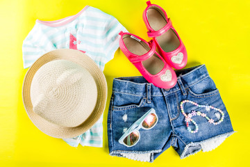 Summer vacation concept, summer child's cloth set - kids shorts, T-shirt, hat, sun glasses, bracelet necklace, sneakers, bright yellow background above flat lay copy space