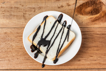 chocolate syrup on white sliced bread on dish, wooden background
