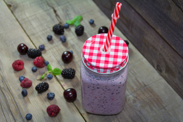 Smoothies in a jar with a lid and a straw. Fruits on a wooden background
