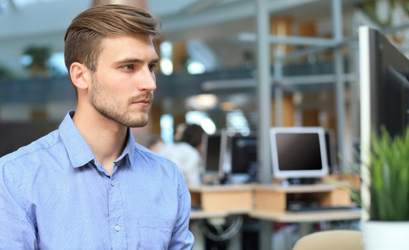 Young man sitting and looking at computer monitor while working in office.