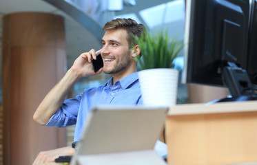 Smiling businessman sitting and using mobile phone in office.