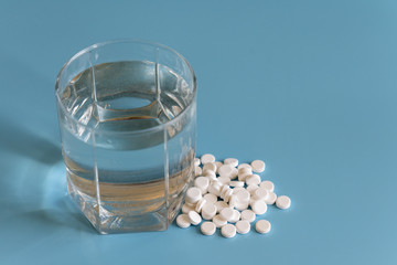 White pills and glass of water on the blue background. Glass of water and pills on blue background
