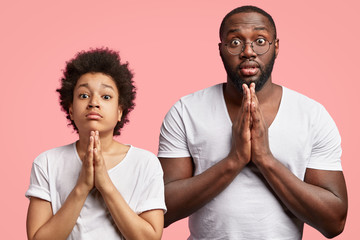 Handsome dark skinned small child with Afro hairstyle and his plump young father pose in praying...