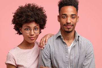 Cropped shot of friendly woman and man companions stand close to each other, look seriously and confidently at camera, listen important information, isolated on pink studio wall, dressed casually