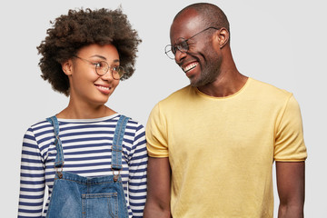 Happy joyful boyfriend and girlfriend have dark skin, look at each other with great love and positiveness, wear casual clothing, isolated over white background. People, relationship and happiness