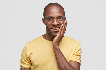 Amazed handsome dark skinned male has charming positive expression, pleasant smile, dressed in casual yellow t shirt, stands on white background, sees something wonderful on stage during perfomance