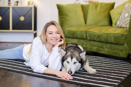 Young woman lying on floor with malamute near sofa. Concept of pets and spending free time at home.
