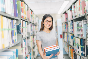 Asian Woman holding a book at bookshelf in the library.