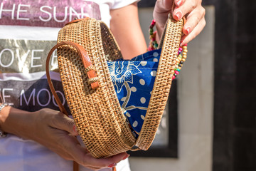 Woman hands with fashionable stylish nude rattan bag. Tropical island of Bali, Indonesia. Rattan handbag.