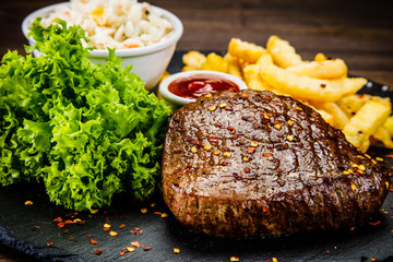 Grilled steak with french fries and vegetables served on black stone on wooden table