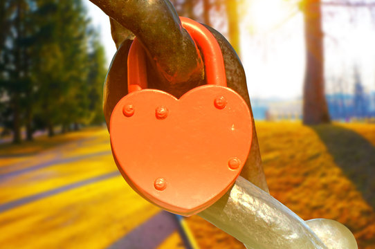 A red heart shaped lock in the sunlight. Sunny day in park on the background.   