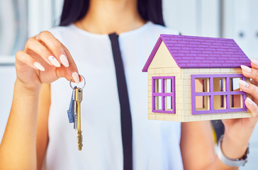 Young businesswoman or real estate agent with hose model and keys in hands closeup.