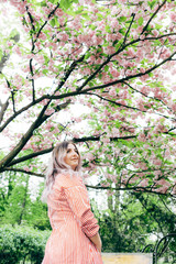Fototapeta na wymiar Beautiful Young Woman Enjoying Sunny Day in Park during Cherry Blossom Season