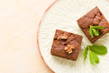 Brownie sweet chocolate dessert with walnuts and meant leaves on craft plate with copy space on pastel beige background.