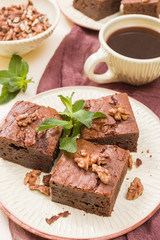 Brownie sweet chocolate dessert with walnuts and meant leaves on craft plate and cup of black coffee.