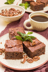 Brownie sweet chocolate dessert with walnuts and meant leaves on craft plate and cup of black coffee.