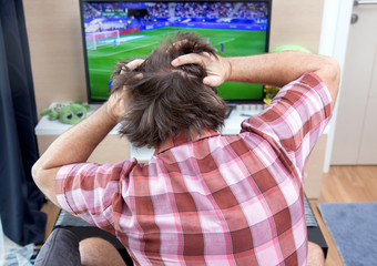 Emotional man watches football in TV. The unhappy disappointed football fan looks at soccer in...