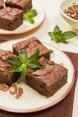 Brownie sweet chocolate dessert with walnuts and meant leaves on craft plate with copy space on pastel beige background.