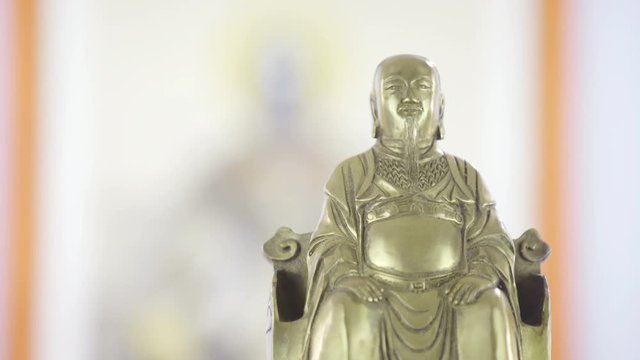Rack focus from Zhang Sanfeng picture to golden statue fat Xuanwu close up 4K. Dolly slide shot focus on big artistic Zhang Sanfeng symbol and refocus to front small golden statue. Sliding from left.