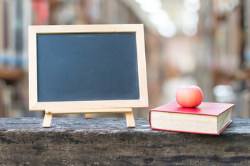 Education concept  with blank black chalkboard stand for announcement with apple, textbook on blur school college library background