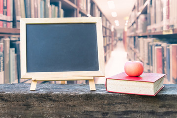 Education concept  with blank black chalkboard stand for announcement with apple, textbook on blur school college library background