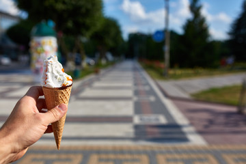 A first person view, a person walking along the road with an ice cream in his hands, shallow depth of field.