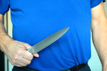 A man holding a kitchen knife in his right hand. Close-up.
