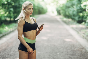 Woman Runner in the Summer Morning Park Listening to Music on Smartphone Using Bluetooth Earphones....