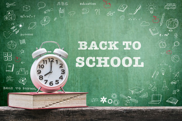 Back to school concept with alarm clock and book on teacher's table and student's doodle drawing on class chalkboard for education announcement
