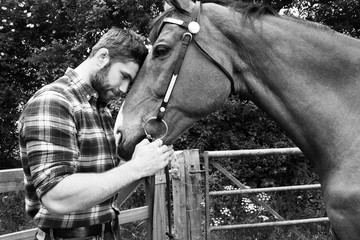 Handsome American cowboy, rider with checked, chequered shirt and jeans pets and loves his horse