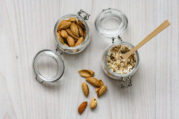 Fototapeta premium Still life of healthy food and diet food, almonds, wooden spoon and muesli in glass jars on a wooden background.
