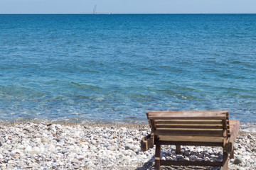 Fototapeta na wymiar Wooden beach chair, sail on the horizon, concept summer vacation