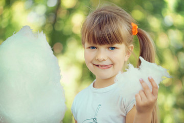 A beautiful naughty little blue-eyed light-blue girl walks in a sunny summer park and eats sweet...
