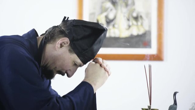 Wisdom and spirituality of Daoist meditation 4K. Long shot of spiritual male person praying to Zhang Sanfeng. Side shot tracking while bowing. Picture of Zhang Sanfeng in background. White studio.